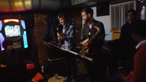 Max Light playing guitar alongside a saxophonist and rhythm section during a live performance at Wally’s Cafe Jazz Club.